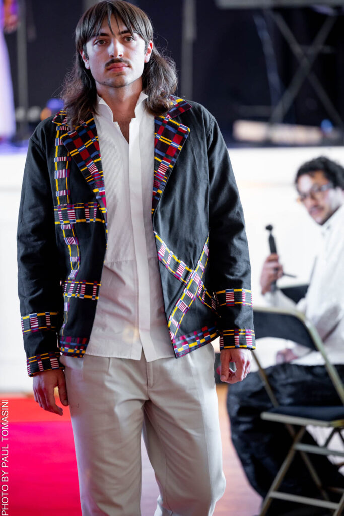 Cet ensemble signé Fatou Touré pour FTY Creations associe une veste en tissu bleu marine rehaussée de broderies colorées à un pantalon fluide ivoire, une silhouette qui allie l'élégance décontractée à l'artisanat traditionnel réinventé, présentée lors du défilé Fashion for Good le 3 juillet 2026.