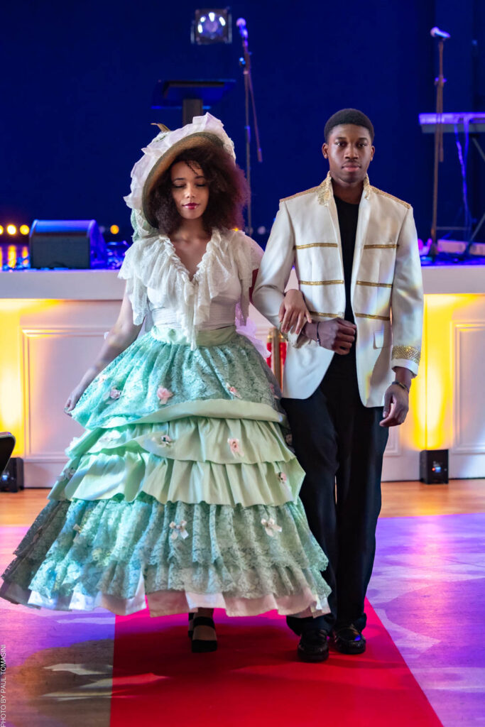 Lors du défilé de Nathalie Froufrou, Alyssa sublime une robe romantique à volants superposés vert d'eau poudré, ornée de fleurs délicates et coiffée d'un large chapeau de paille victorien, tandis que Moussa qui l'accompagne dans un smoking blanc rehaussé de galons dorés, incarnant ensemble un saisissant dialogue entre nostalgie couture et modernité.