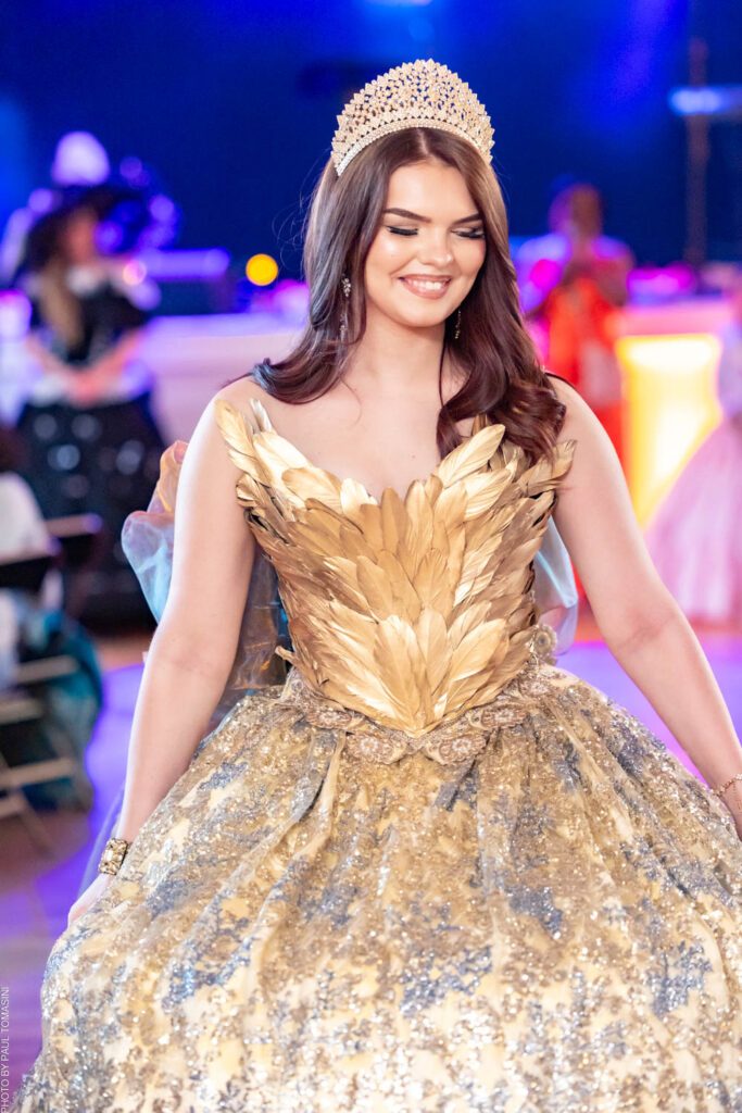 Corset à mi-chemin entre la mythologie grecque et le siècle de Louis XIV, Sur le podium, un éclat : celui d'une robe de bal où l'or des plumes répondait à l'argent des paillettes, portée par Ludivine, princesse d'un soir en diadème.